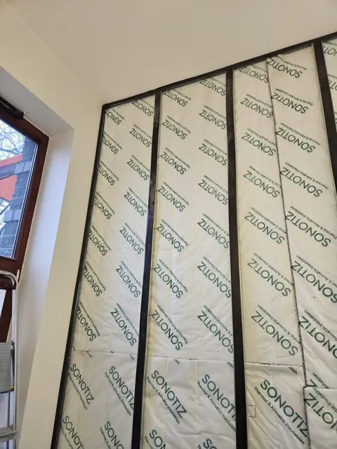Ruszt i maty akustyczne na ścianie przy oknie